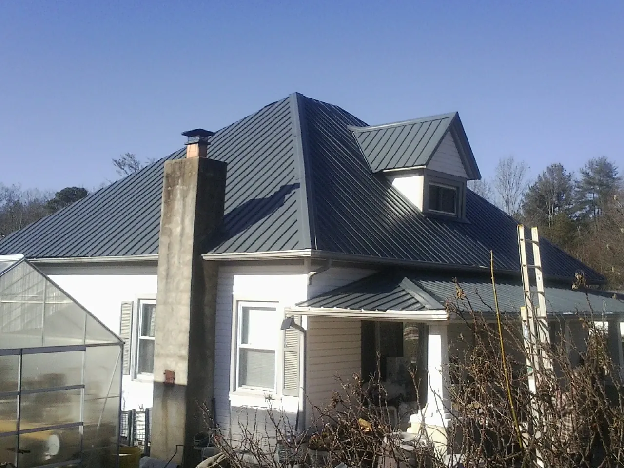 Dark blue standing seam metal roof on a white farmhouse with dormer — Slate & Tile Roof Repair by Roofing Brothers in Fairburn