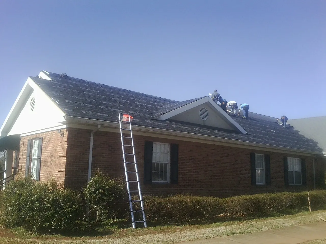 Crew tearing shingles off a brick ranch roof with a ladder set — Metal Roof Repair work by our crew in Fairburn