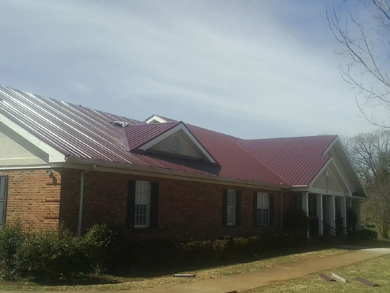 Red metal roof with gabled entries on a long brick building, from a Hail Damage Roof Repair job in Fairburn