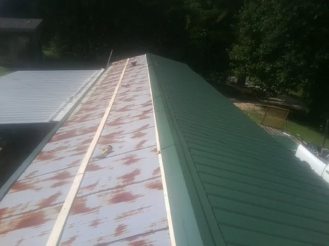 Old rusted panels beside newly installed green metal roofing — Wind Damage Roof Repair by Roofing Brothers in Fairburn