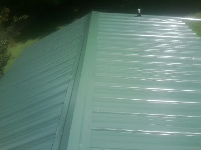New green metal panels meeting at the ridge of a roof — Flat Roof Repair work by our crew in Fairburn