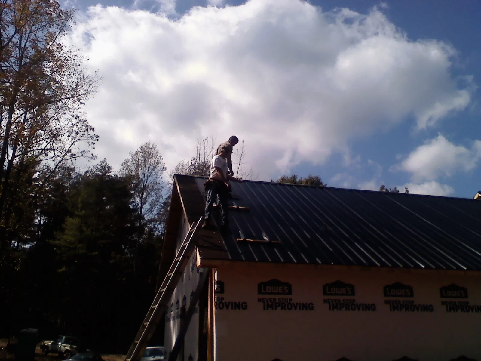 Roofer fastening dark metal panels high against a cloudy sky, from a Roof Inspection job in Fairburn