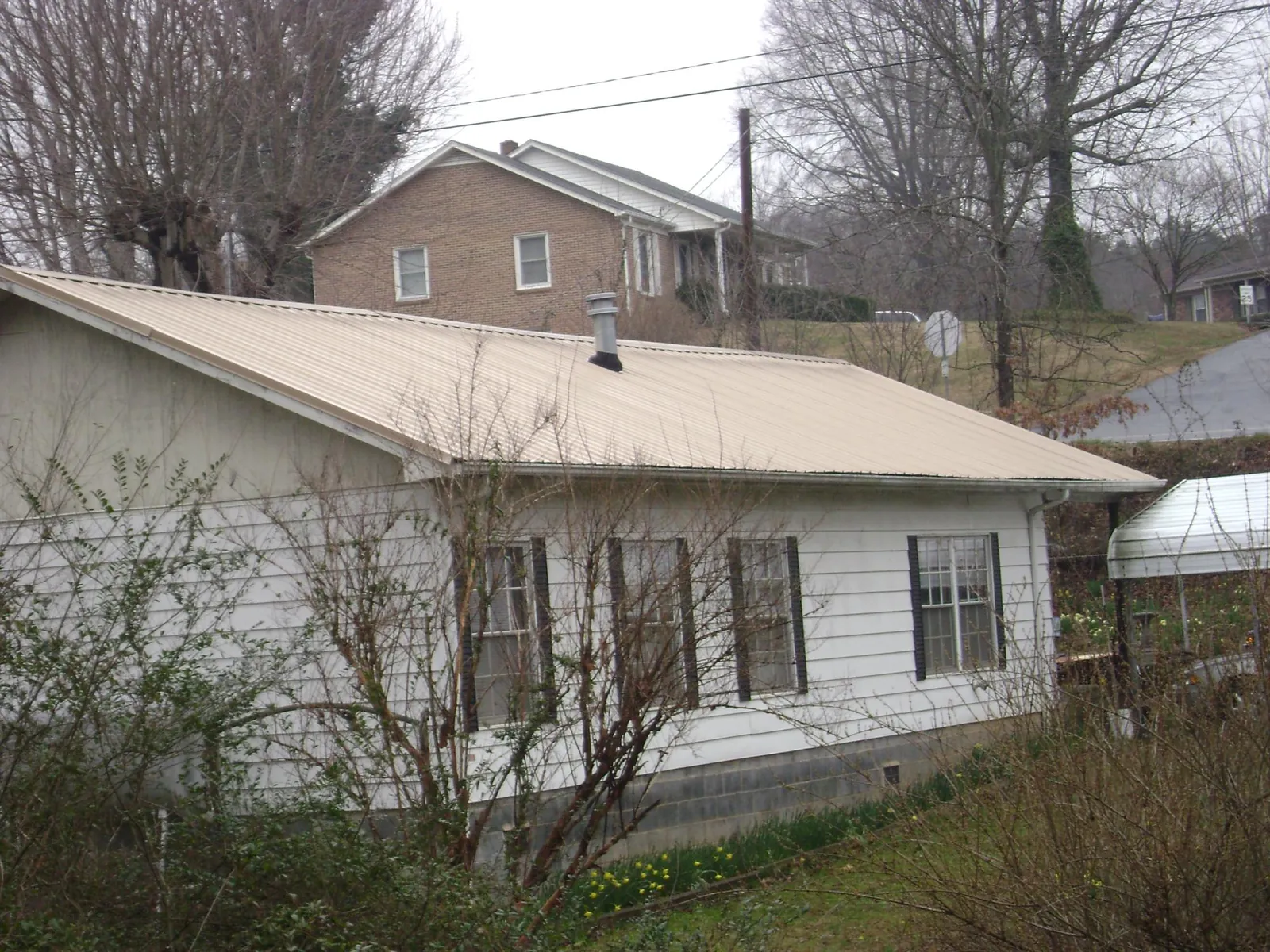 Tan metal roof on a white sided house set into a hillside — Commercial Roofing by Roofing Brothers in Fairburn